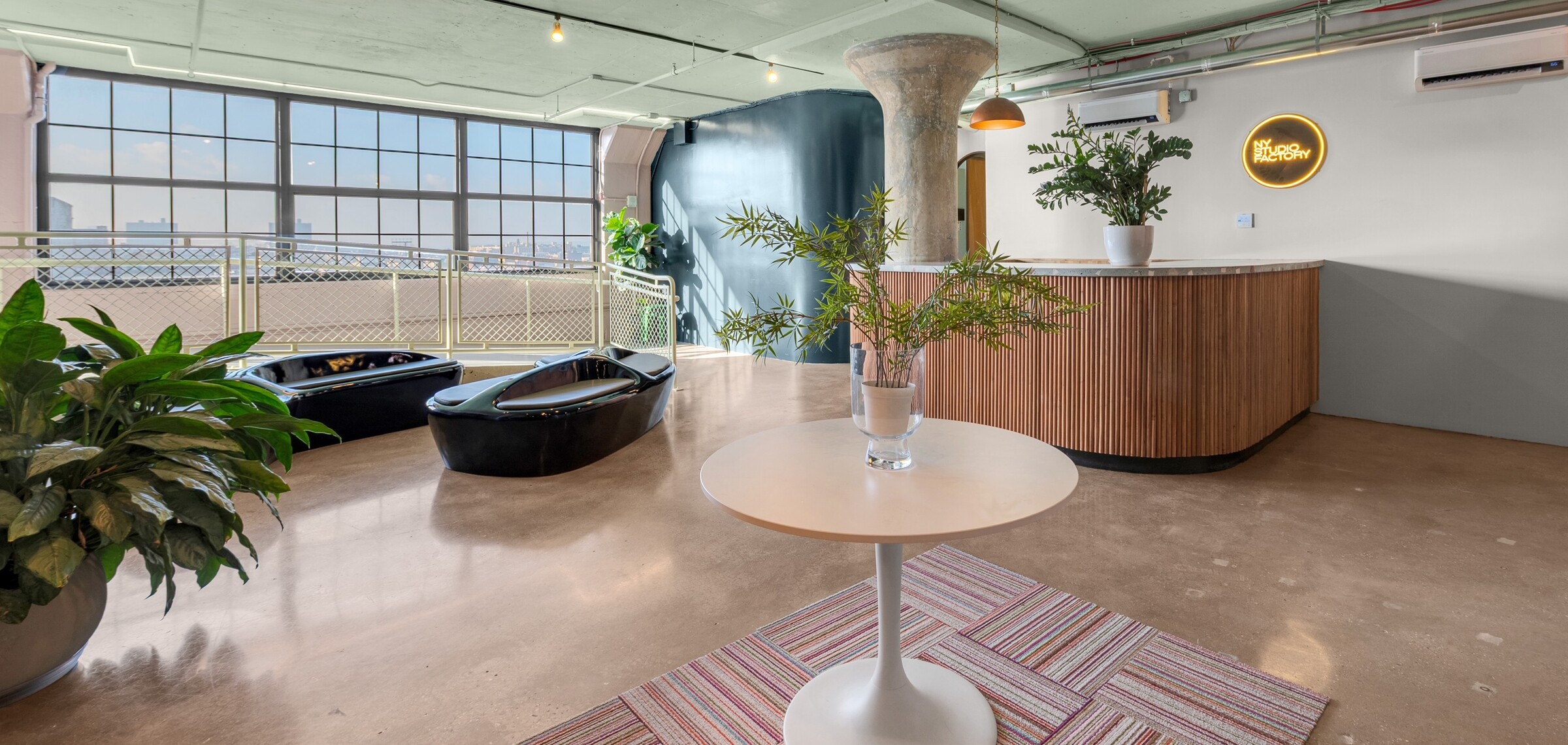 NYSF lounge — NYSF neon sign on the white wall, curved column, skyline windows, and pod seating