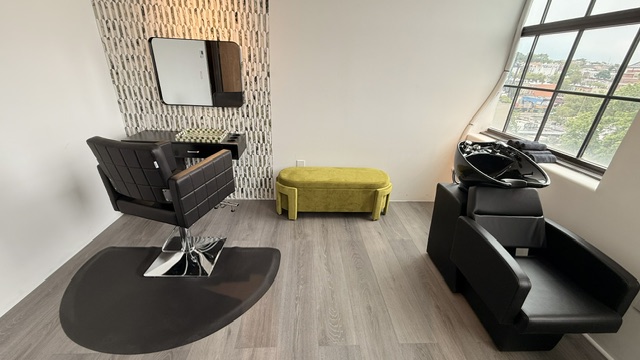 Hair Studio: reverse-angle wide with styling chair foreground, wash bowl to the right, yellow ottoman.