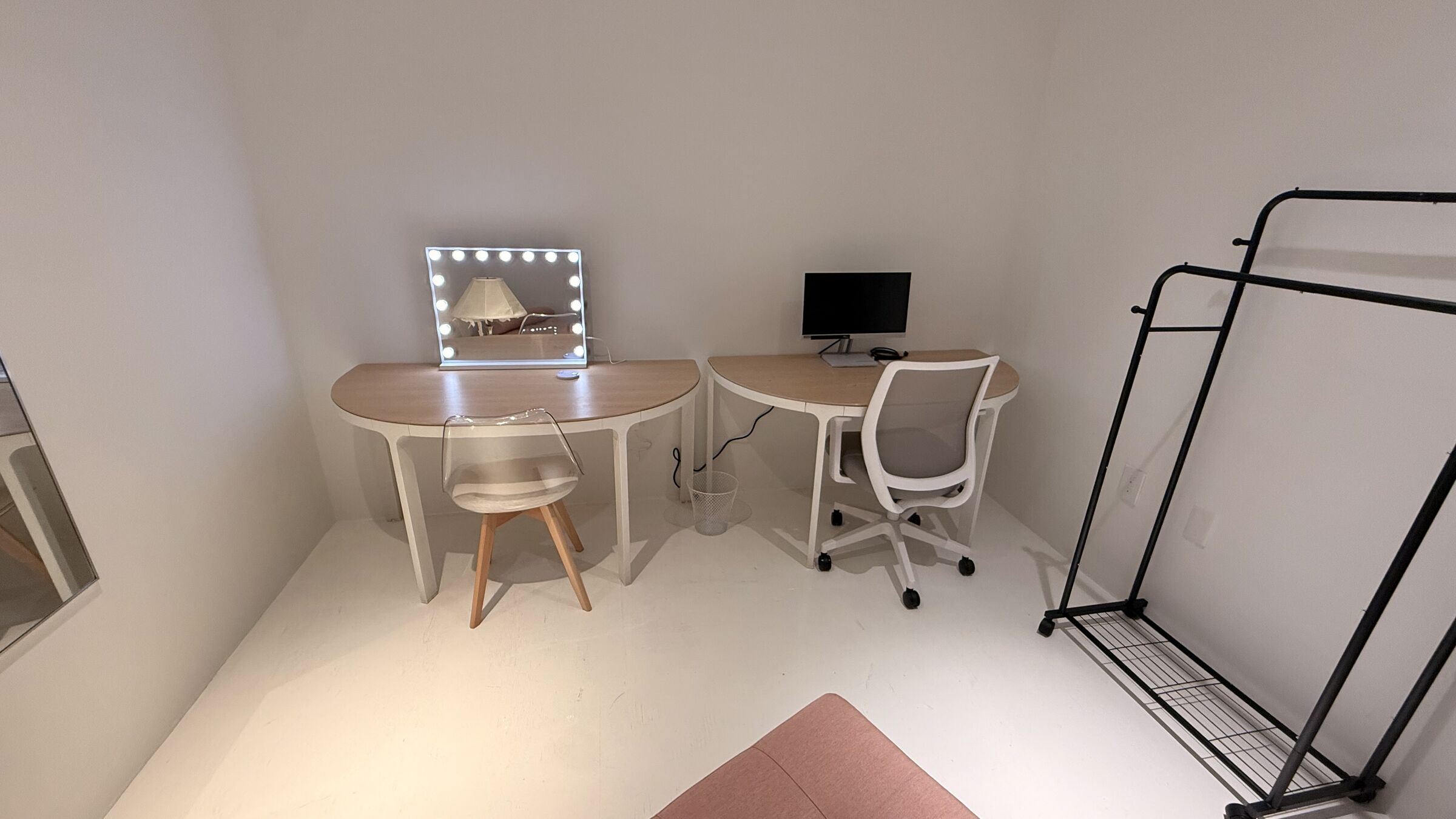 The Makeup Studio: eye-level view of the lit Hollywood-style vanity, half-moon desks with monitor, and clothing rack at right.