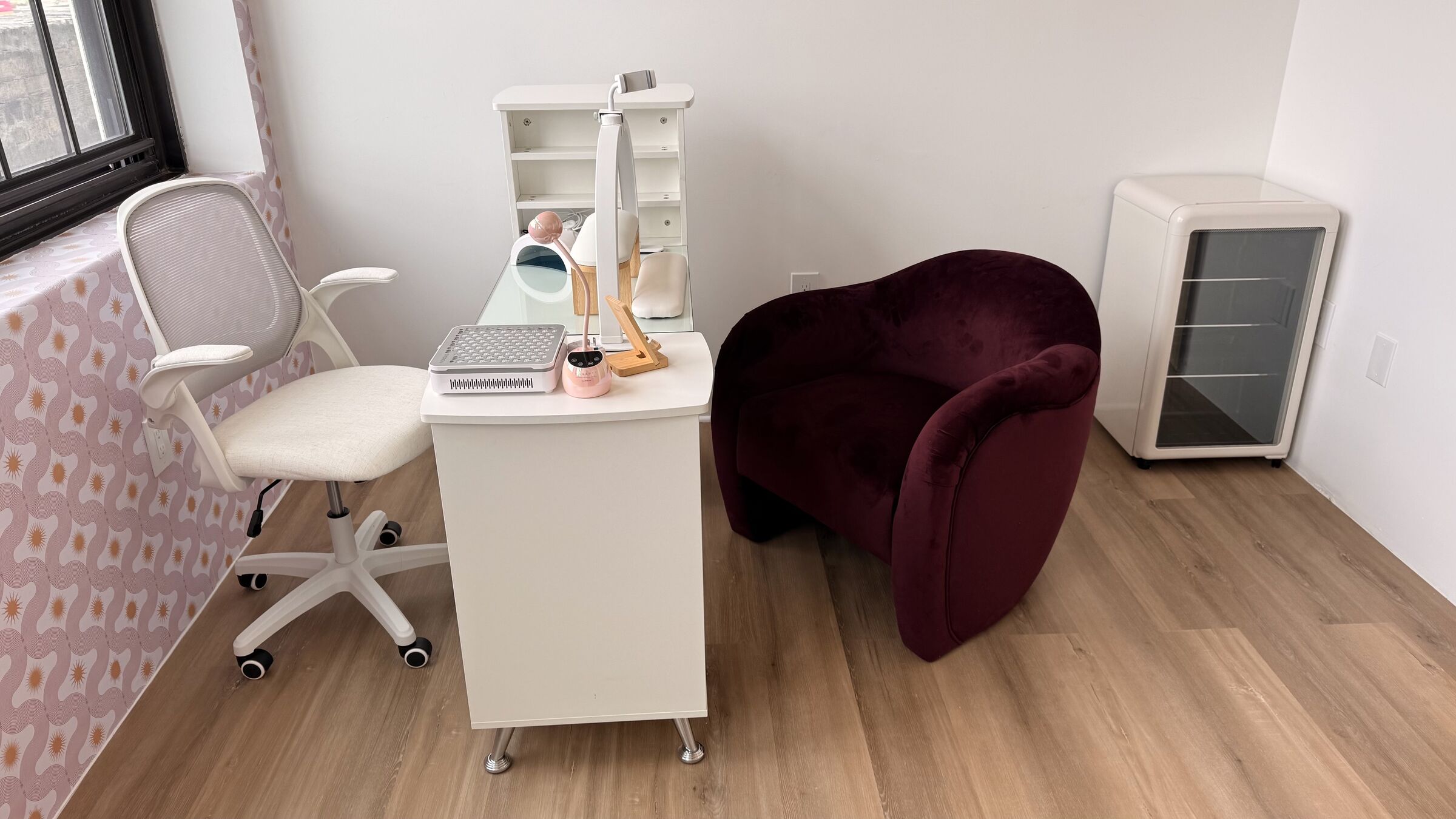 Nail Studio: white manicure desk with gel lamp, LED dryer, and dust extractor; pink-orange accent wall, burgundy velvet client chair, hardwood floor.