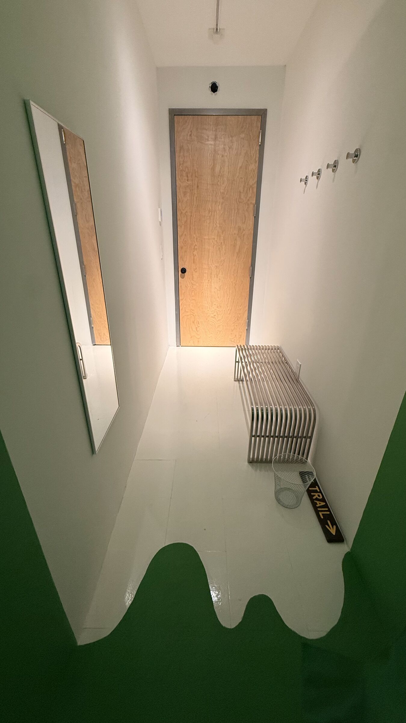 The Stage anteroom — white walls with a stainless steel bench, green floor drip leading into the chroma chamber, and a 'TRAIL →' sign on the floor.